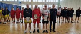 wyróżnieni czterej sportowcy w piłce siatkowej stoją w szeregu na boisku w hali sportowej, za nimi pozostali zawodnicy