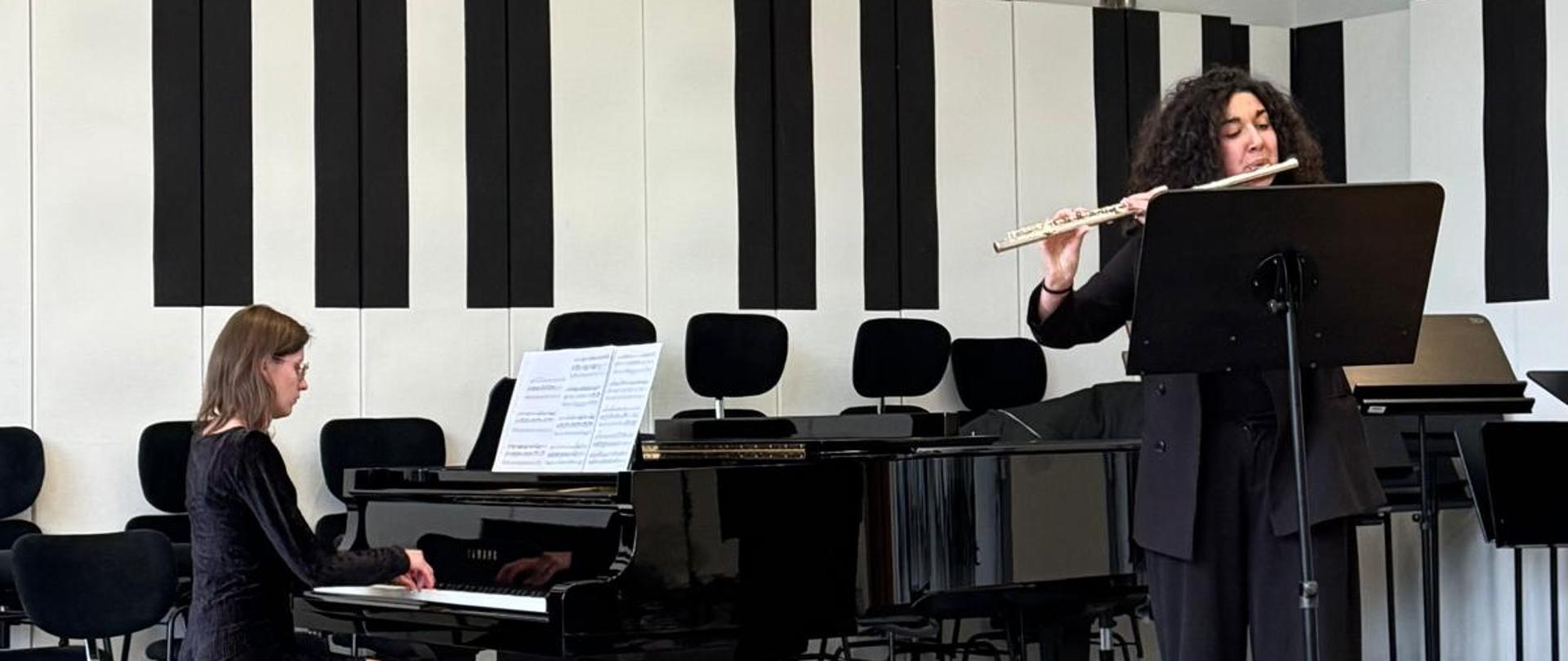 Dziewczyna gra na flecie, kobieta jej akompaniuje.