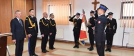 Na zdjęciu widzimy gości honorowych Wojewodę i Komendantów Wojewódzkich PSP w mundurach strażackich. Przed nimi stoi strażak w mundurze reprezentacyjnym. Na zdjęciu jest również poczet sztandarowy w 3 osobowym składzie salutujący w mundurze reprezentacyjnym.