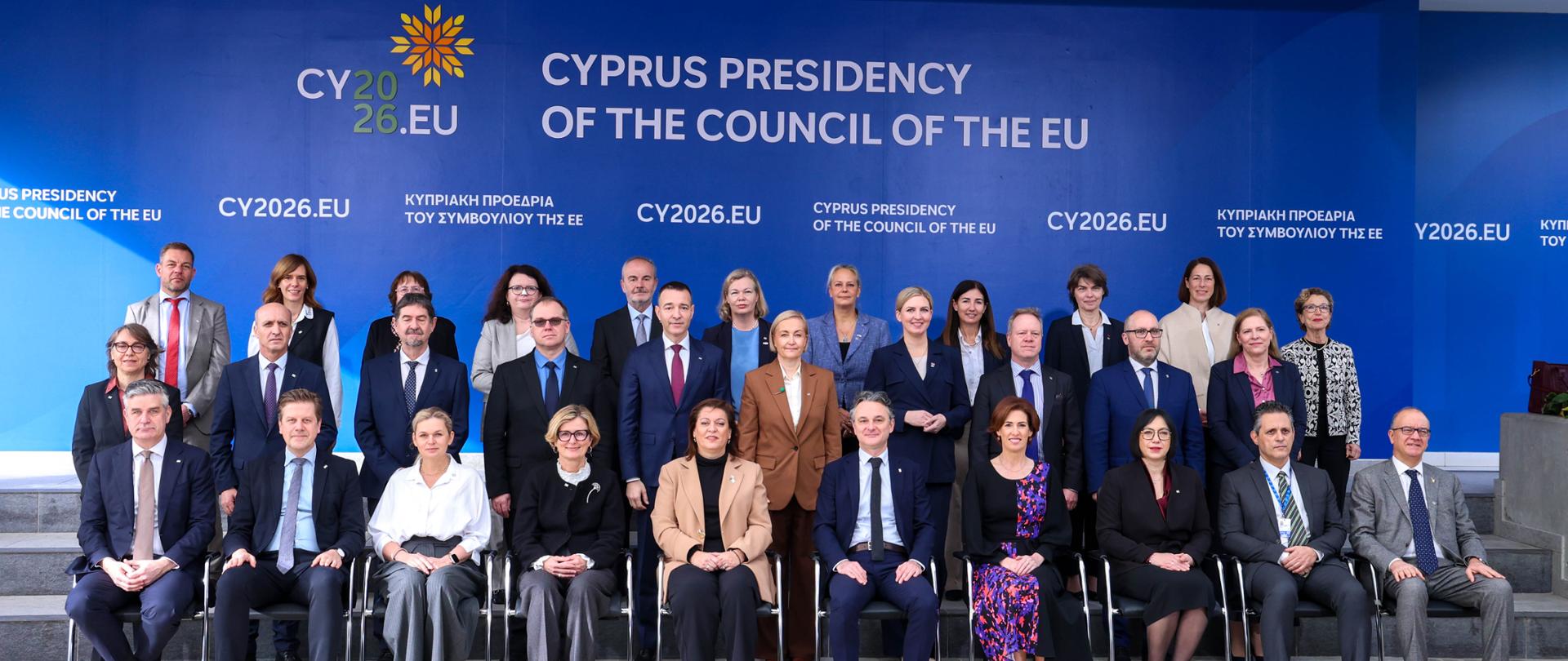 Zdjęcie grupowe uczestników nieformalnego posiedzenia Rady UE na Cyprze. Na zdjęciu widać kilkanaście osób - ministrów i innych uczestników posiedzenia - ubranych w eleganckie stroje. W tle logo cypryjskiej prezydencji Unii Europejskiej oraz link do domeny prezydencji.