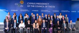 Zdjęcie grupowe uczestników nieformalnego posiedzenia Rady UE na Cyprze. Na zdjęciu widać kilkanaście osób - ministrów i innych uczestników posiedzenia - ubranych w eleganckie stroje. W tle logo cypryjskiej prezydencji Unii Europejskiej oraz link do domeny prezydencji.