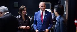 Na pierwszym planie widoczne są dwie osoby - mężczyzna i kobieta, witające gościa festiwalu. 