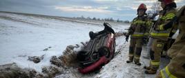 Samochód osobowy na dachu w rowie a obok strażacy
