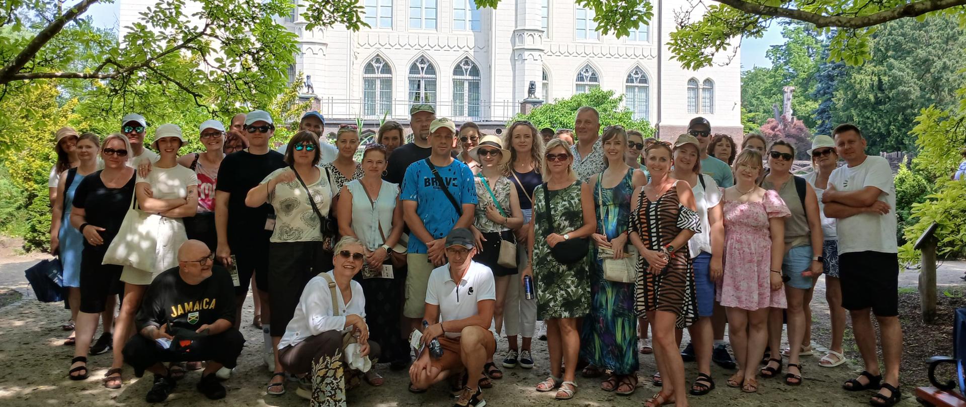 Grupa kilkudziesięciu inspektorów pozująca do zdjęcia w zacienionym miejscu pod dużymi drzewami, w tle zamek w Kórniku
