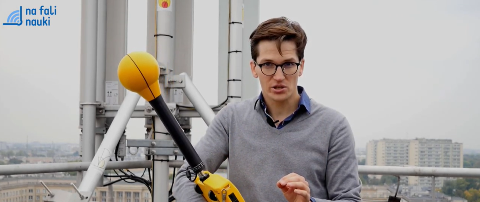 Bohater reportażu stoi w pobliżu stacji bazowej z miernikiem w ręce