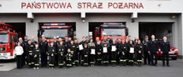 Na zdjęciu widzimy komendantów PSP, władze lokalne, prezesów OSP wraz z dziećmi z młodzieżowych drużyn pożarniczych pozujących do zdjęcia grupowego na tle budynku komendy PSP.