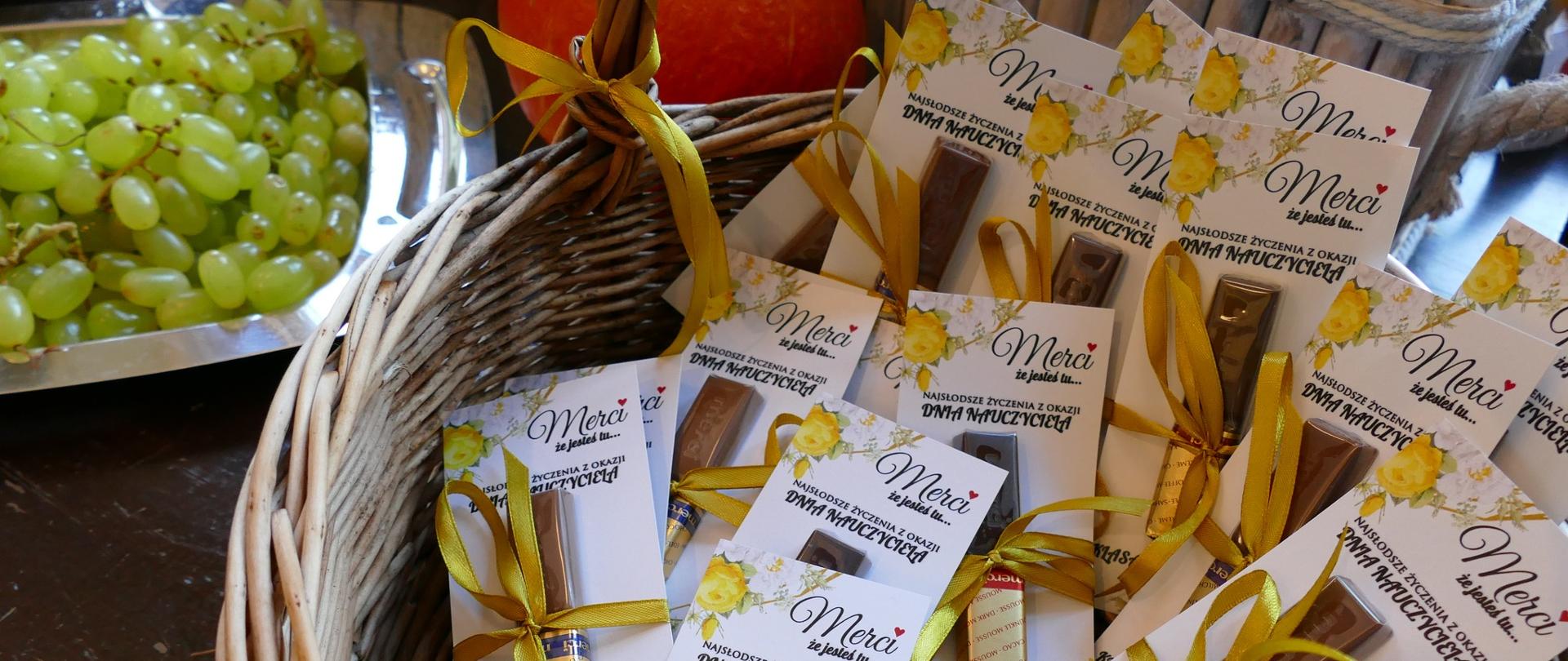 Dzień edukacji narodowej 2022 Zielone winogrona na srebrnej tacy w lewym górnym rogu zdjęcia, resztę zdjęcia zajmuje wiklinowy kosz z przewiązanymi złotą wstążeczką merci 