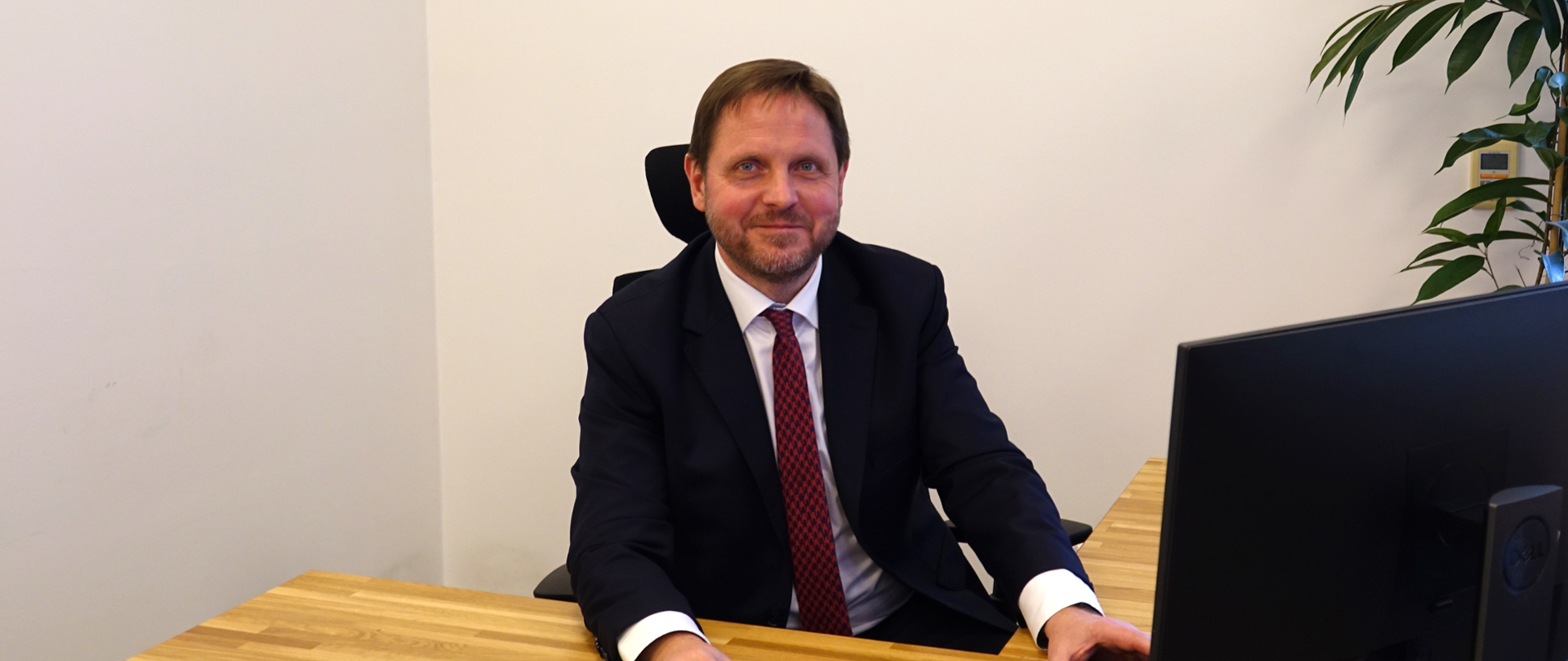 Mężczyzna w garniturze, siedzący za biurkiem, przy komputerze 