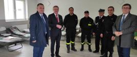 Przedstawiciel władzy rządowej oraz samorządowej w towarzystwie komendanta powiatowego i druhów strażaków w trakcie dokonywania przeglądu pomieszczeń i wyposażenia przygotowanego dla uchodźców