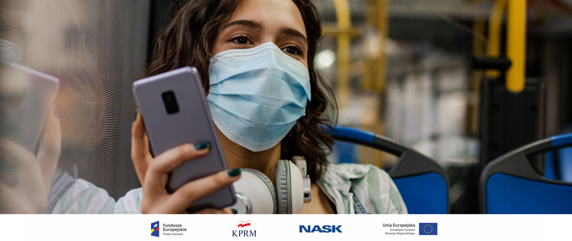 Kobieta w maseczce, jadąca miejskim autobusem, w dłoni trzyma smartfona.