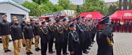 Zdjęcie przedstawia pododdziały strażaków ustawione do odznaczeń na tle pojazdów pożarniczych oraz czerwone namioty z logo Państwowej Straży Pożarnej.