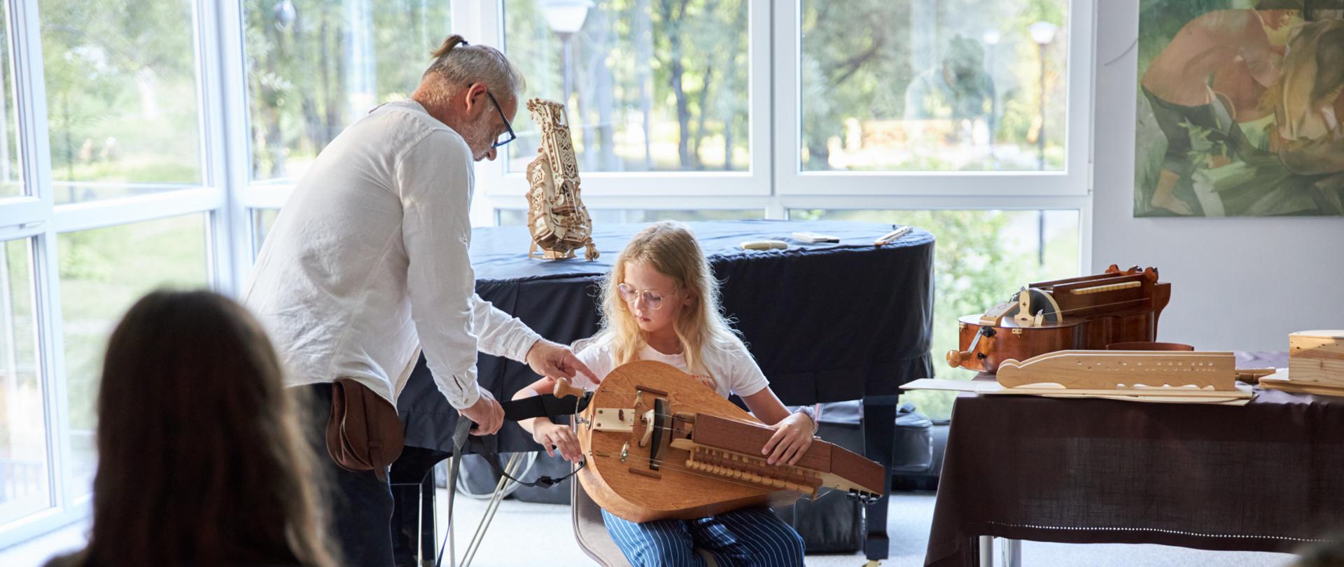 zdjęcie uczniowie siedzą na krzesłach , uczennica trzyma lirę, obok prowadzący warsztaty