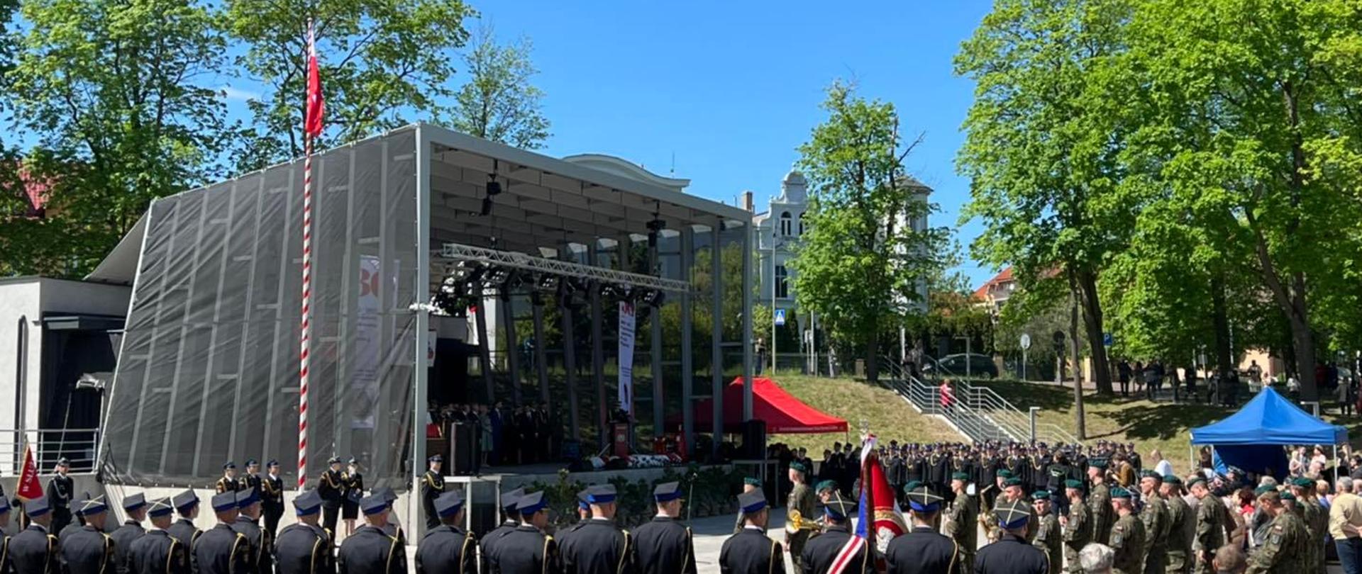 Pododdziały PSP oraz OSP widoczne przed sceną amfiteatru w Łobzie, na zdjęciu również orkiestra wojskowa. Widoczny masz flagowy z wciągniętą flagą.