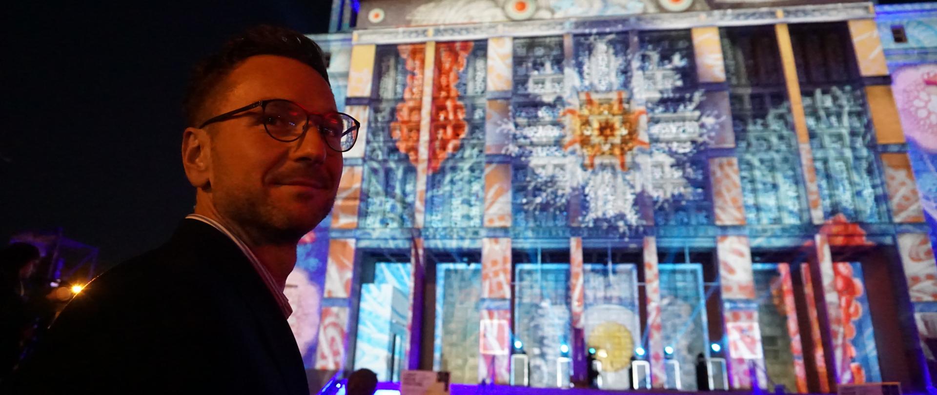 Minister Waldemar Buda na tle podświetlonego budynku.