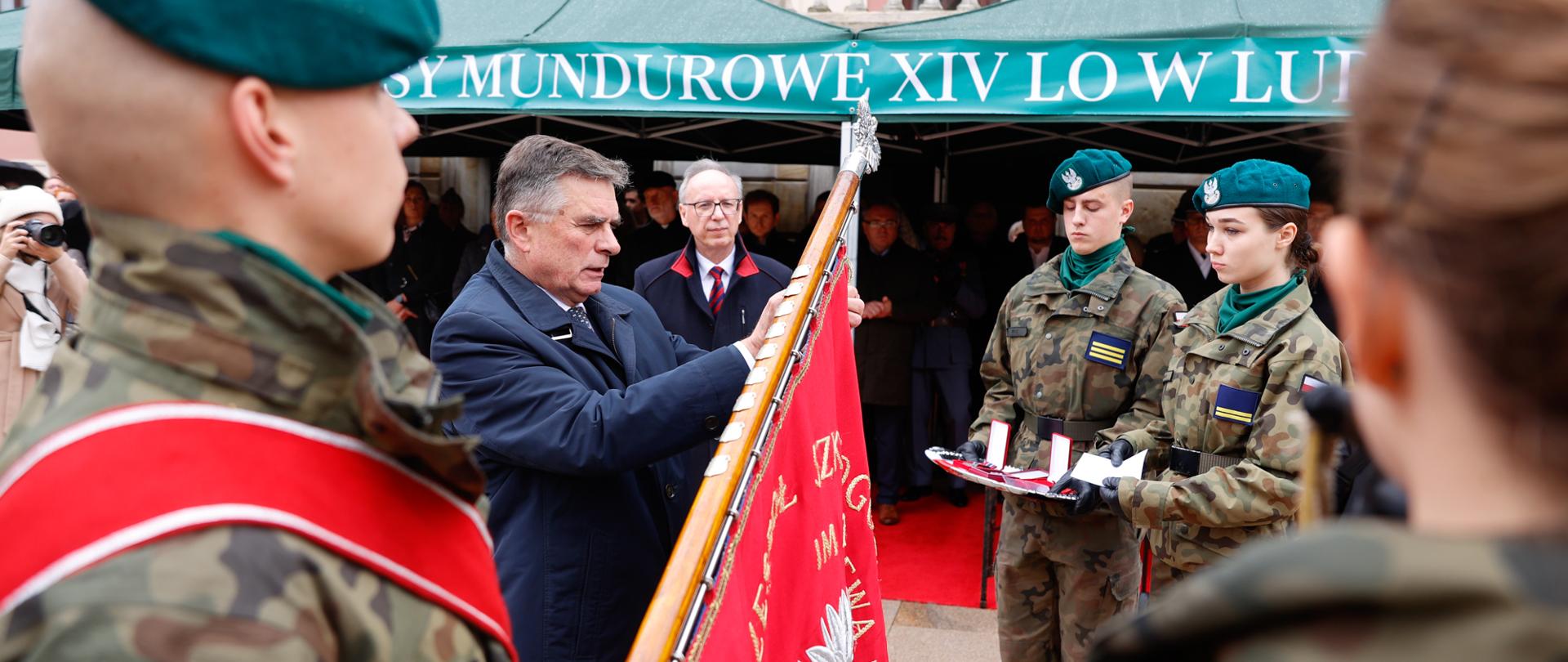 Wojewoda przypina Medal na sztandar. Obok niego uczniowie klas wojskowych.