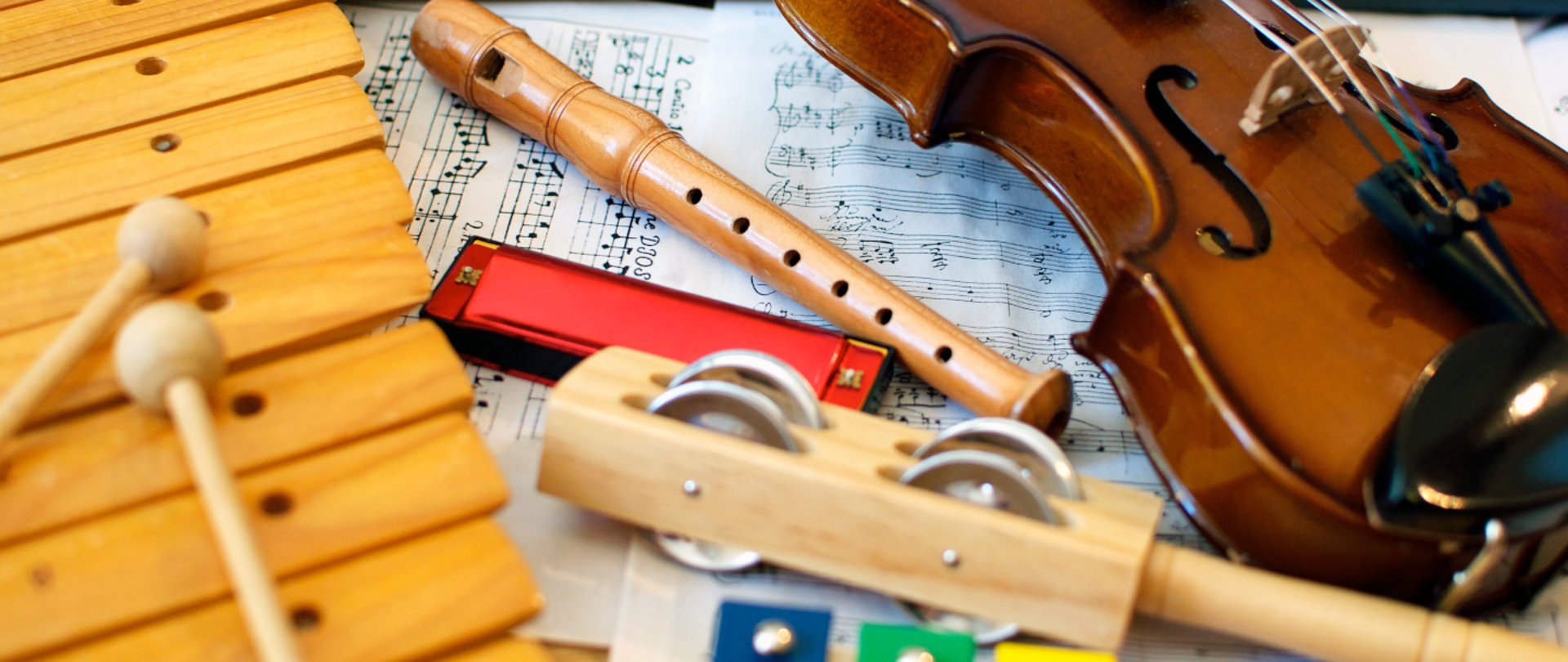 Zdjęcie przedstawia instrumenty muzyczne: skrzypce, flet prosty, harmonijkę ustną oraz instrumenty perkusyjne na tle zapisu nutowego.