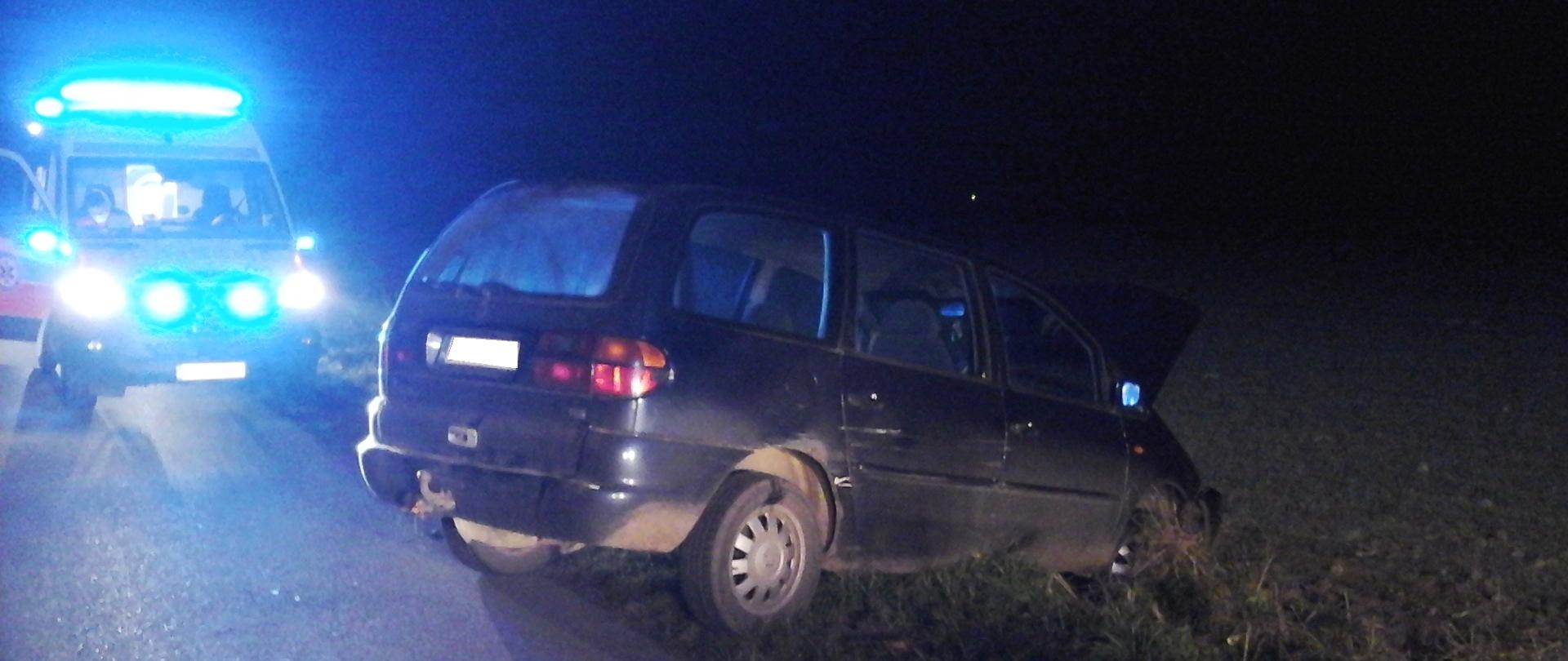 Samochód osobowy VW Sharan stojący na poboczu jezdni. W tle karetko pogotowia ratunkowego z włączonymi światłami uprzywilejowania.