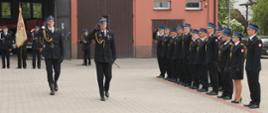 Zdjęcie przedstawia uroczyste obchody Dnia Strażaka z udziałem funkcjonariuszy Państwowej i Ochotniczej Straży Pożarnej podczas apelu na placu przed wewnętrznym komendy. Widoczni są strażacy w mundurach galowych, poczet sztandarowy oraz uczestnicy ceremonii i zaproszeni goście.