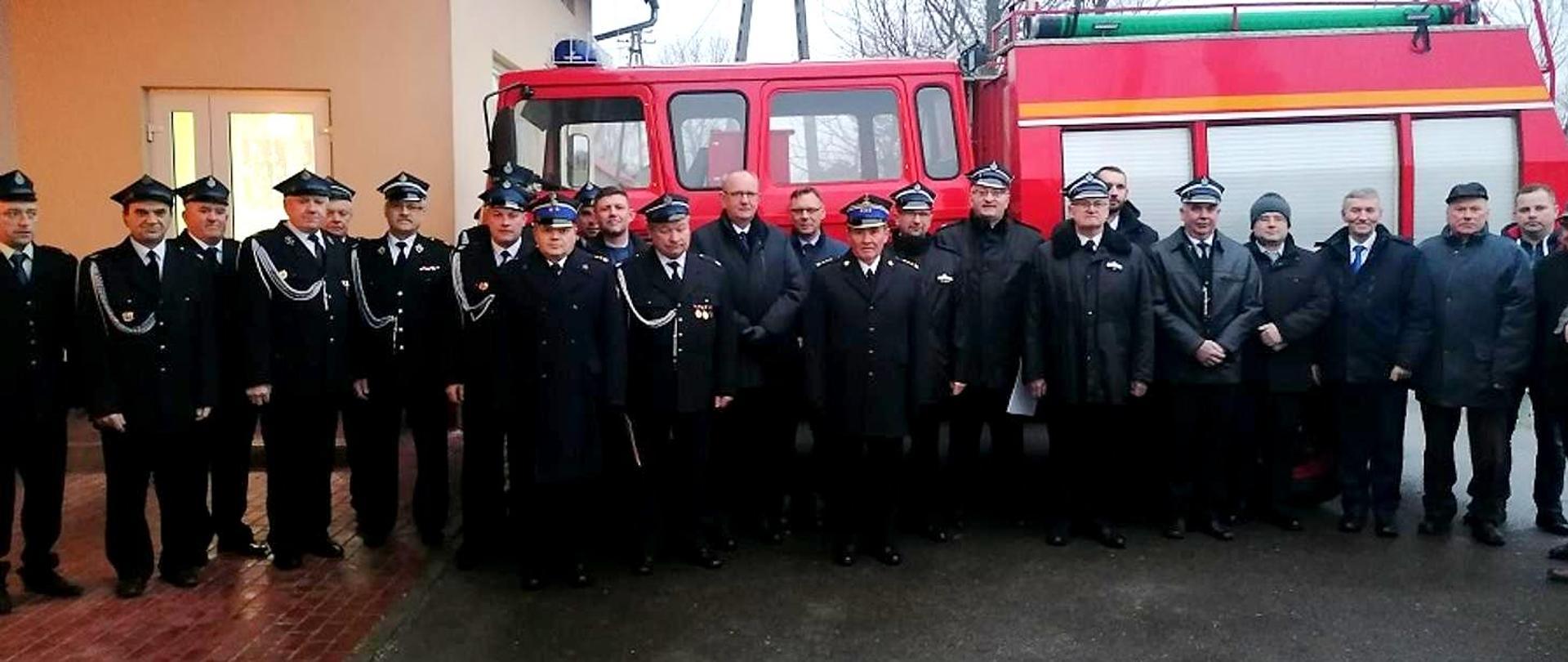 Na fotografii uwieczniona uroczystość przekazania samochodu dla OSP Wola Otałęska. Zdjęcie grupowe na tle przekazanego samochodu ratowniczo-gaśniczego Przed remizą na placu zgromadzili się druhny i druhowie oraz zaproszeni goście. Strażacy ubrani w umundurowania galowe koloru granatowego z okryciem na głowie typu czapki rogatywki.