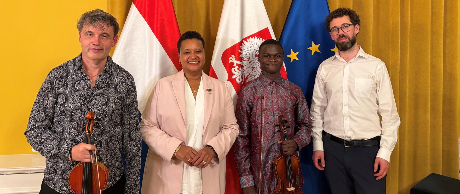 Pamiątkowe zdjęcie z koncertu w Ambasadzie RP w Hadze. Cztery osoby stoją obok siebie, zwrócone w stronę obiektywu. Od lewej: Michał Buczkowski, Ambasador RP Margareta Kassangana, Stephen Otieno oraz Andrew Wright

