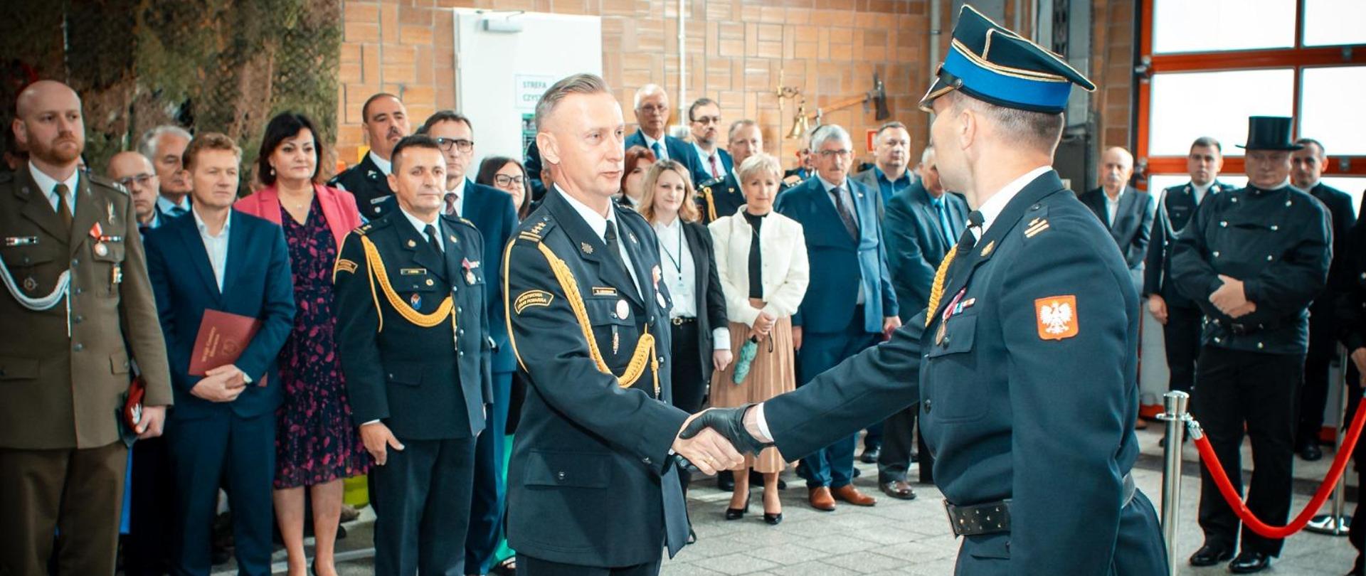 Obchody Dnia Strażaka 2024 r. - Dowódca Uroczystości mł. bryg. Piotr Markiewicz składający meldunek st. bryg. Damianowi Legierskiemu - Zastępcy Śląskiego Komendanta Wojewódzkiego o gotowości do rozpoczęcia uroczystych obchodów. W tle zaproszeni goście na trybunie honorowej.