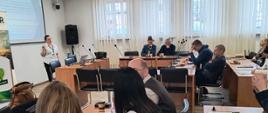 Grupa osób siedzących przy stolach oraz słuchających prelekcji na szkoleniu
