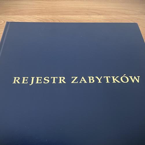 granatowa okładka księgi z dużym napisem złotymi literami "REJESTR ZABYTKÓW"