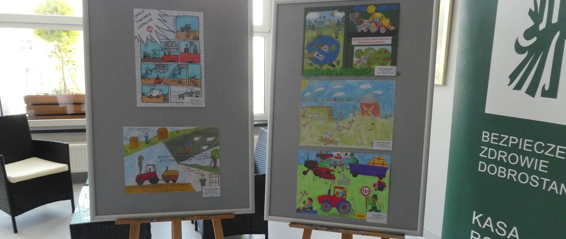 Na dwóch sztalugach stoją nagrodzone prace plastyczne, obok rollup KRUS