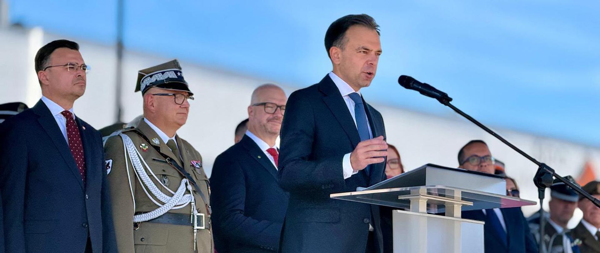Min. A. Domański przemawiający z mównicy z polskim godłem. Na drugim planie goście zaproszeni na obchody, w tym oficerowie Wojska Polskiego