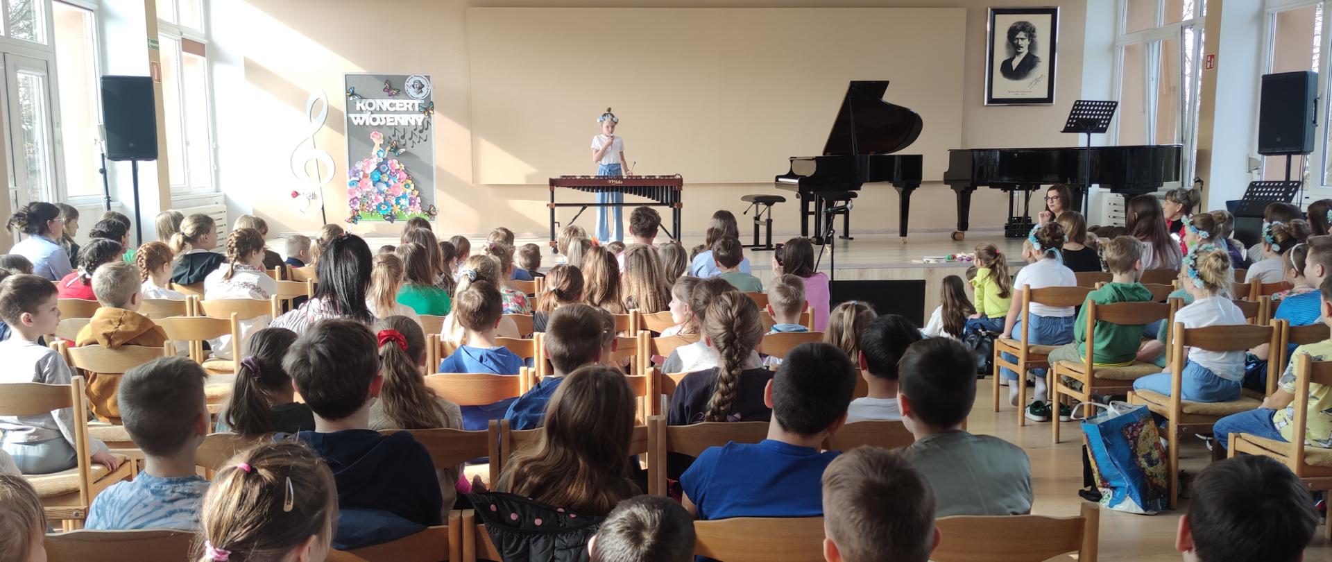 na scenie grająca uczennica na ksylofonie, na widowni siedzące dzieci