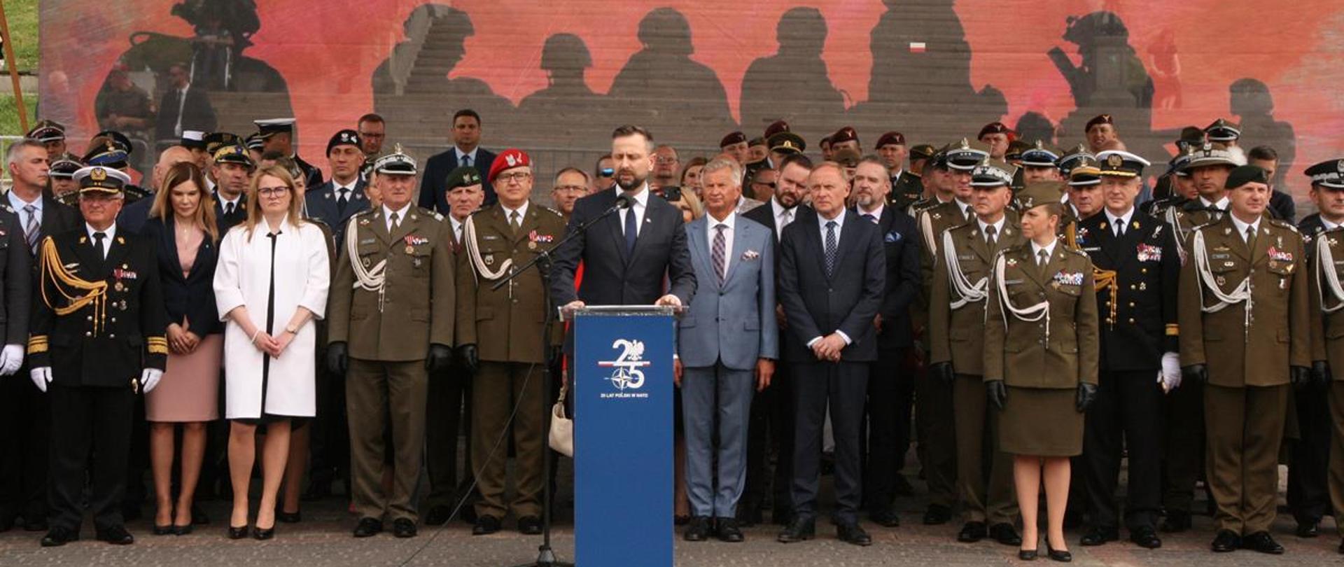 Na zdjęciu widać zaproszonych gości podczas przemówienia ministra ON. W tle biało czerwona flaga z napisem Dzień Weterana