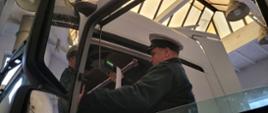 Umundurowany funkcjonariusz kujawsko-pomorskiej Inspekcji Transportu Drogowego stoi w wejściu do kabiny ciągnika siodłowego. Inspektor sporządza wydruk z tachografu cyfrowego.