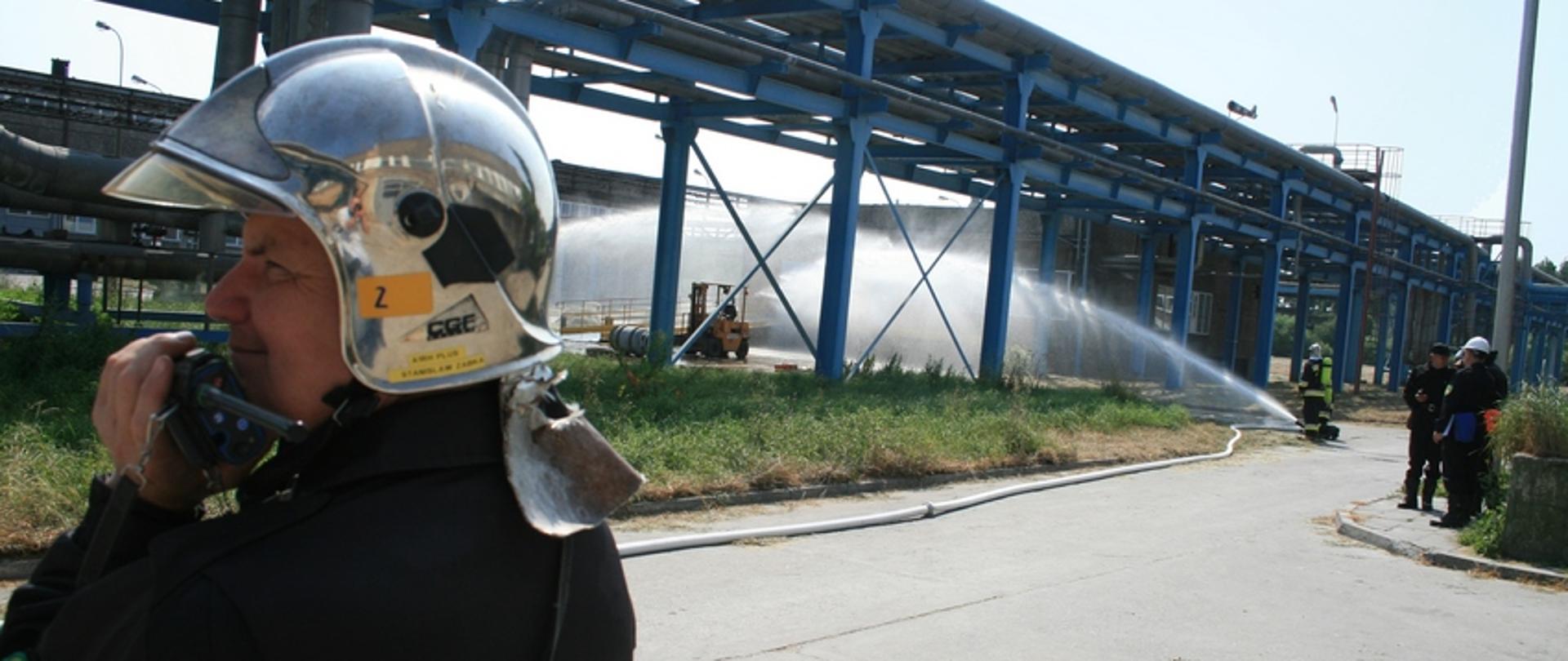 Zdjęcie przedstawia strażaka rozmawiającego przez radio przy rurociągu