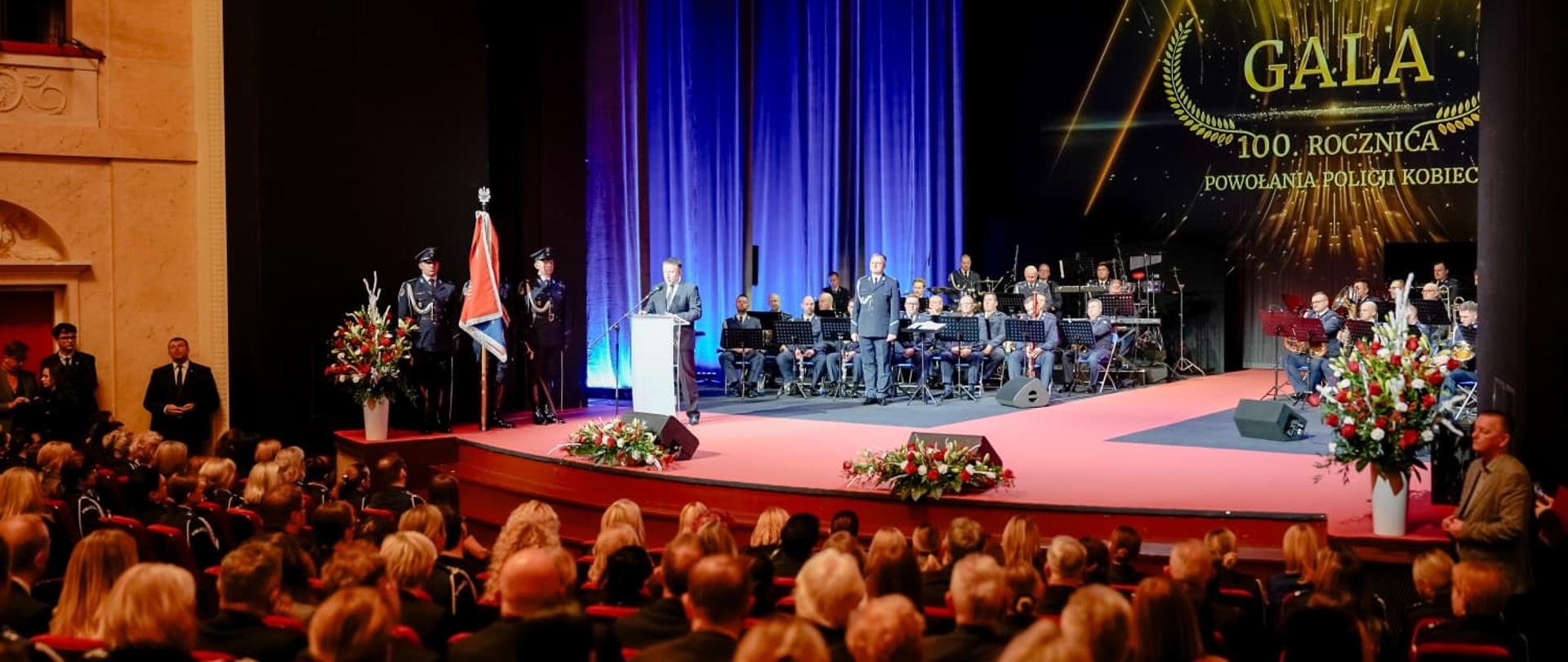 Uroczysta gala. Widownia ludzi, na scenie orkiestra.