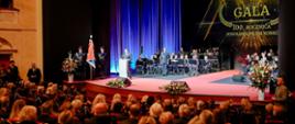 Uroczysta gala. Widownia ludzi, na scenie orkiestra.