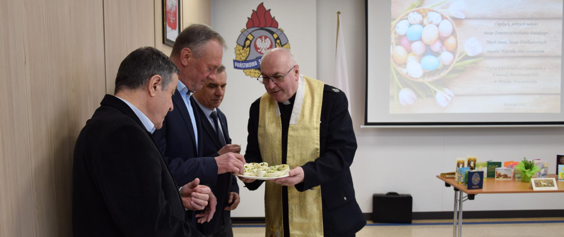 Dh ks. Zenon Wójcik rozdaje świąteczne jajka zaproszonym gościom i składa świąteczne życzenia.