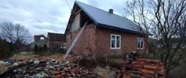 Zdjęcie przedstawia budynek mieszkalny jednorodzinny. W wyniku silnego wiatru uszkodzeniu uległy ściany szczytowe budynku. Cegły leżą przy budynku. 