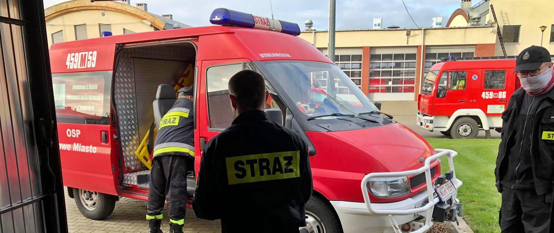 Zdjęcie przedstawia dystrybucje środków ochrony osobistej otrzymanych z Urzędu Wojewódzkiego. Na zdjęciu znajduje się trzech strażaków ubranych w ubrania koszarowe. w tle znajduje się budynek KOmendy oraz samochody pożarnicze.