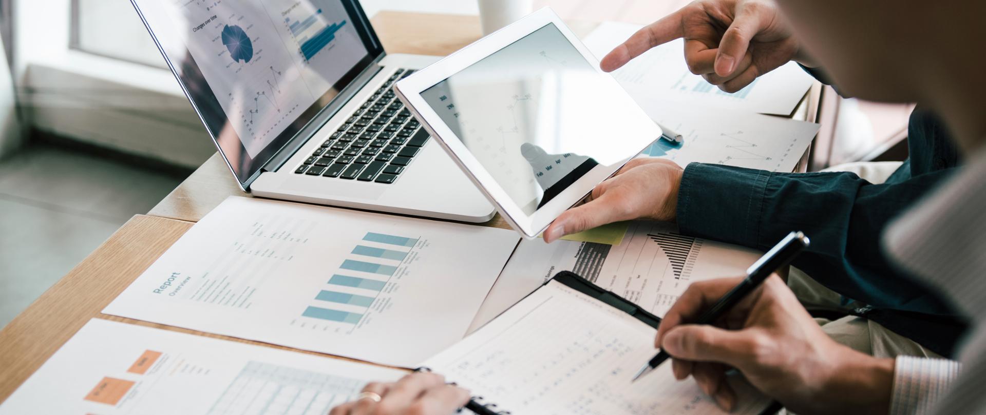 Business partnership coworkers using a tablet to analysis graph company financial budget report and cost work progress and planning for future in office room.