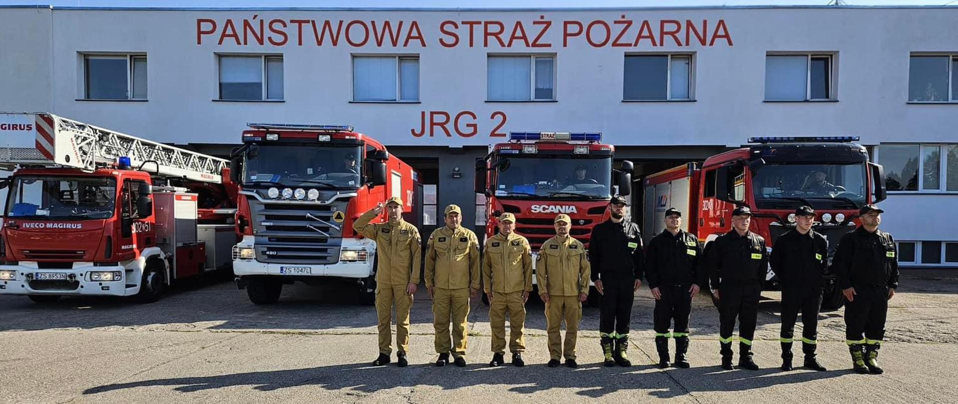 Strażacy z Jednostki Ratowniczo Gaśniczej nr 2 KM PSP w Szczecinie przed jednostką, w tle widoczne wozy pożarnicze. 