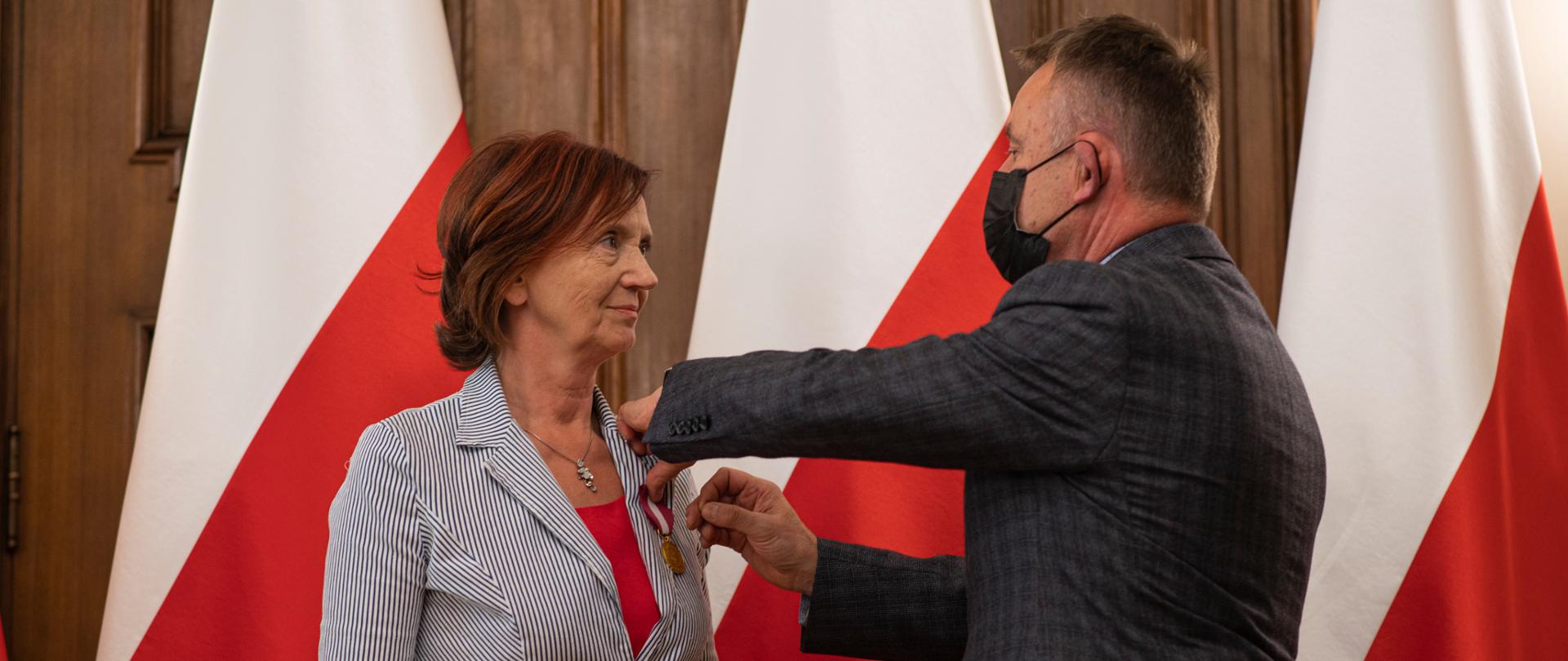 Wicewojewoda łódzki odznacza wyróżnionego pracownika na tle biało-czerwonych flag
