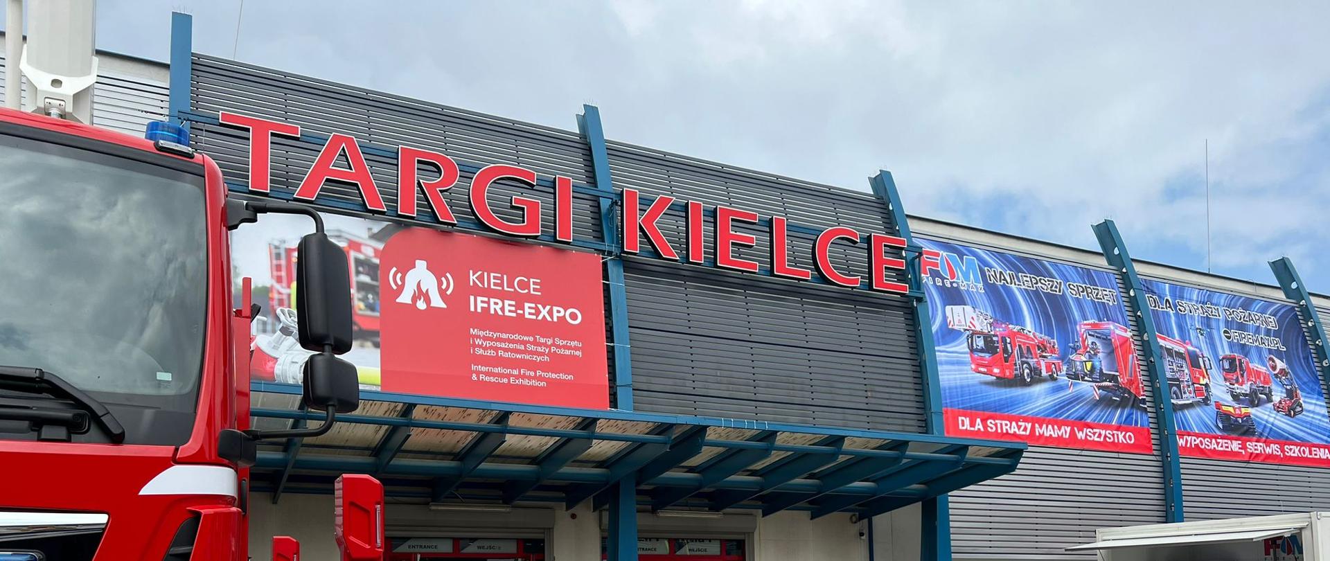 Budynek z szyldem Targi Kielce , przed którym stoją osoby i samochód ratowniczy straży pożarnej