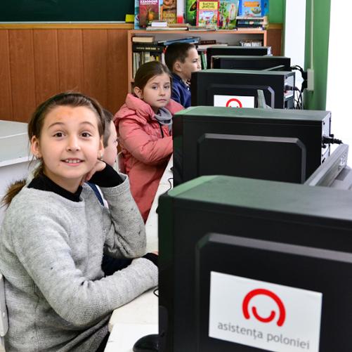 dzieci siedzące przy komputerach oznakowanyc znakiem Polska pomoc