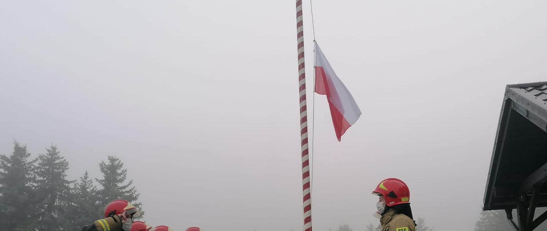 uroczysta zmiana służbowa podczas wciągnięcia flagi. Na zdjęciu dwie zmiany służbowe ubrane w umundurowanie specjalne dokonuje zmiany służbowej, trzech ratowników stoi przy maszcie i wciągają flagę. 