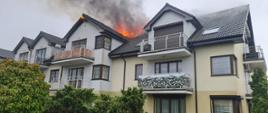 Zdjęcie przedstawia budynek wielorodzinny z widocznymi płomieniami na dachu.
