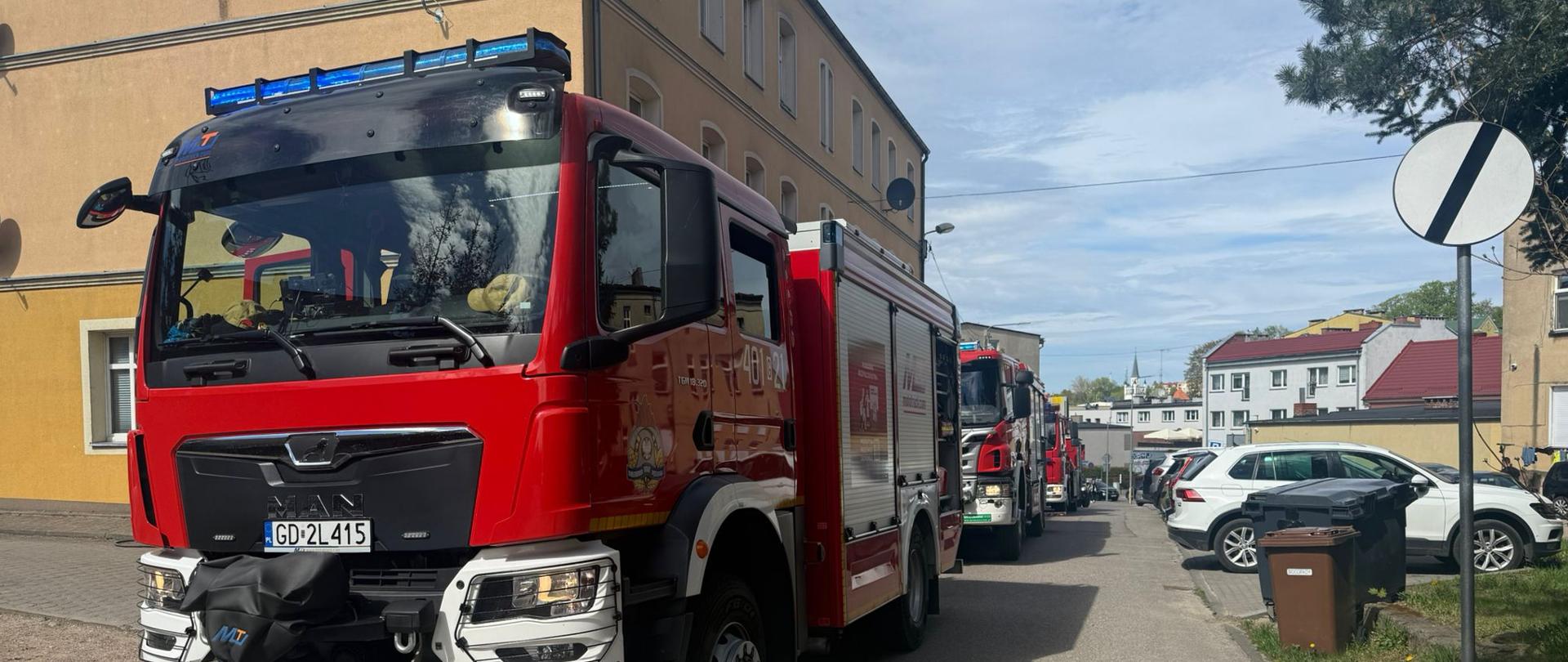 Czerwony wóz strażacki stoi na drodze, w tle żółty budynek.