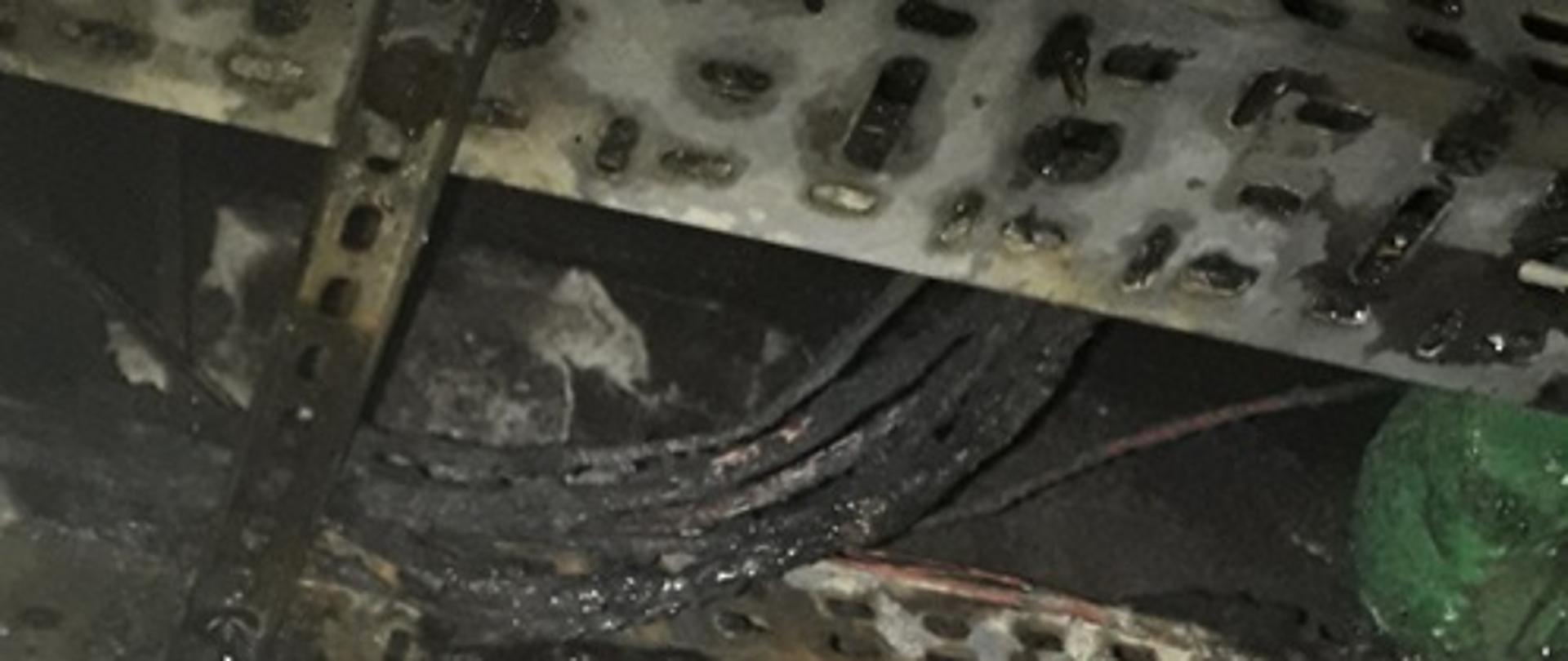Na zdjęciu spalona plastikowa rozdzielnia. U góry na zdjęciu widać spalone przewody elektryczne w tunelu kablowym
