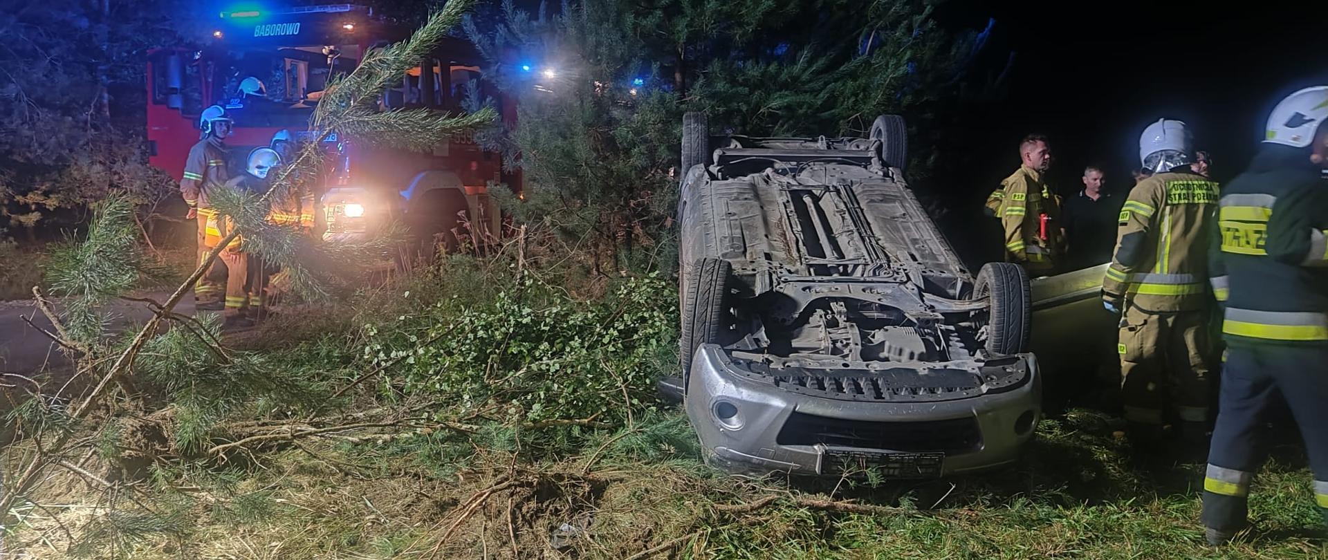 Samochód po dachowaniu na poboczu, strażacy w pobliżu