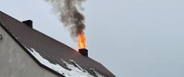Dom jednorodzinny. W komina wydobywa się ogień oraz kłęby dymu.