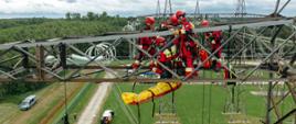 Zdjęcie zrobione na zewnątrz, podczas ćwiczeń strażaków na słupie wysokiego napięcia. Strażacy ze specjalistycznej grupy ratownictwa wysokościowego realizują epizod ćwiczeń.